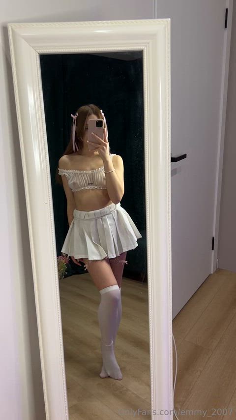 Cute brunette in sheer top and white skirt playing in the mirror thumbnail