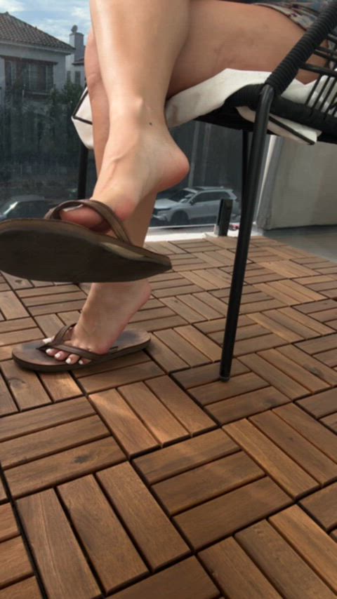 he camera catches me lost in my own little moment — gently swinging my rainbow flip-flops at the edge of my toes. The bright colors glimmer with each tiny movement, perfectly showing off my fresh white pedicure. Every time my foot dangles, the flip-flop threatens to fall, only for me to catch it again with a teasing flex. It’s slow, playful, and completely effortless — like I know you’re watching but pretending not to notice. My toes peek out, the glossy white polish glowing against the soft lig thumbnail